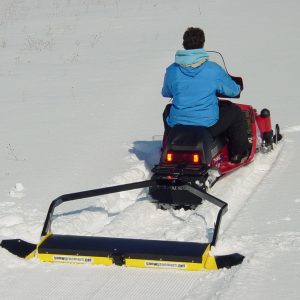 snow groomer towed by small snowmobile
